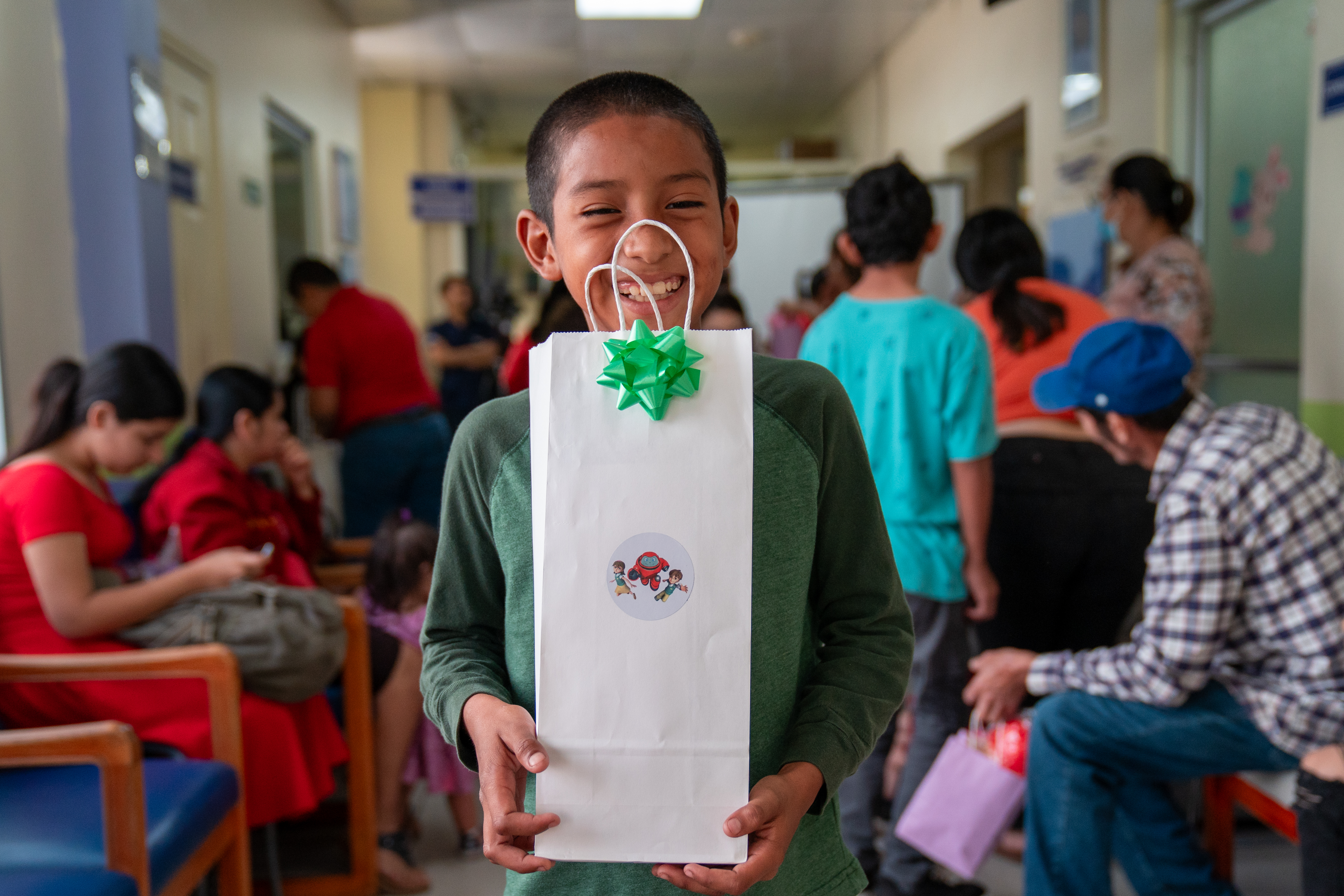 A young boy at Ruth Paz Hospital smiles as he holds up a gift bag from the Superbook team.