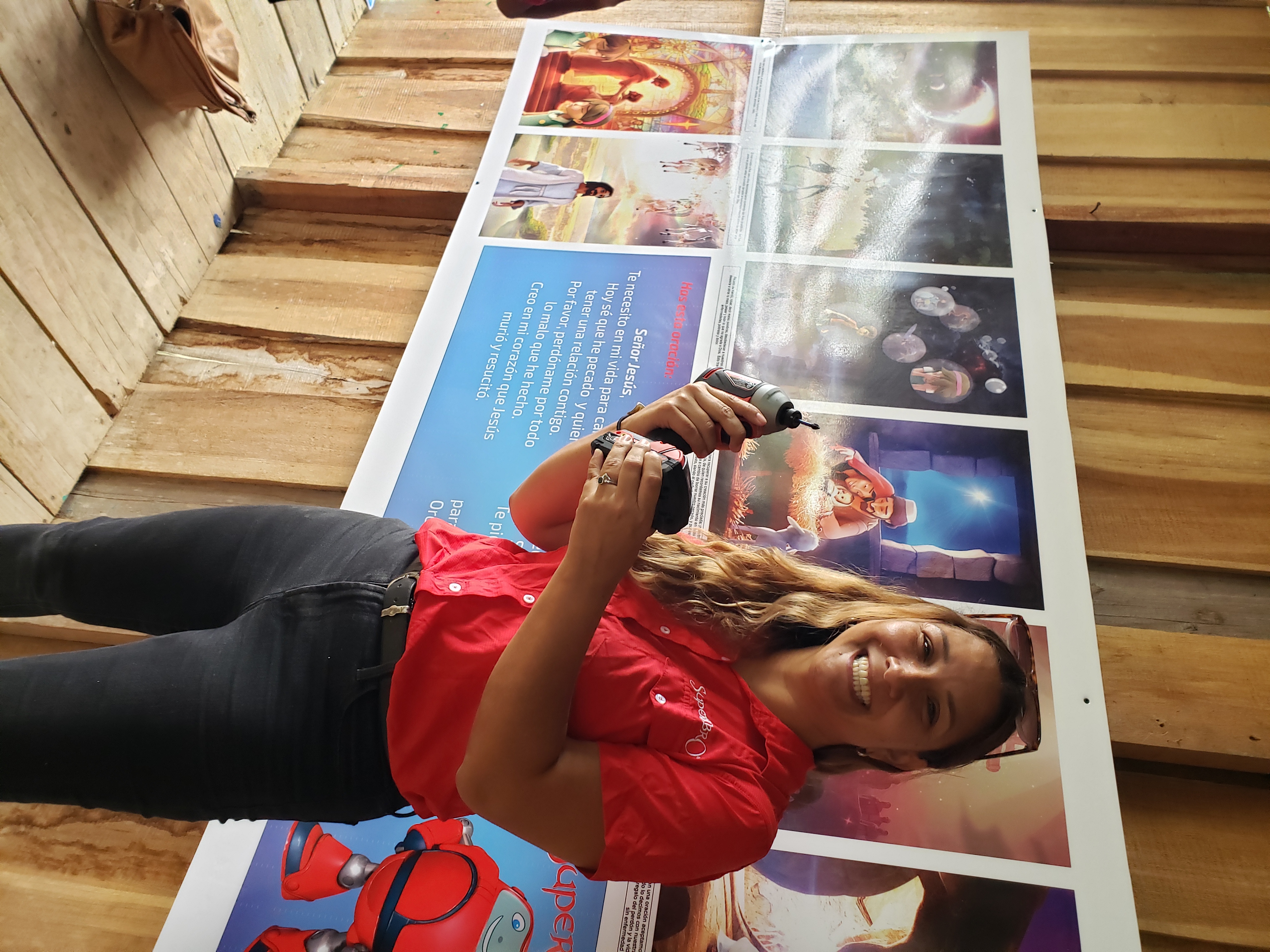 A Superbook Team member holds up a drill in front of the mural she just secured to the schoolhouse wall.
