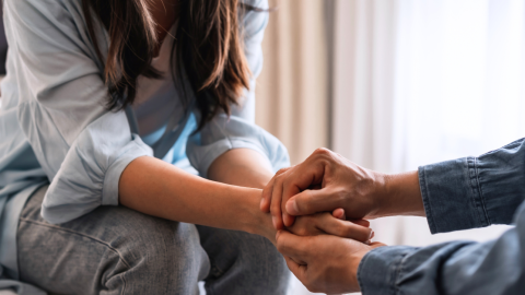 man comforting woman by holding her hands in his